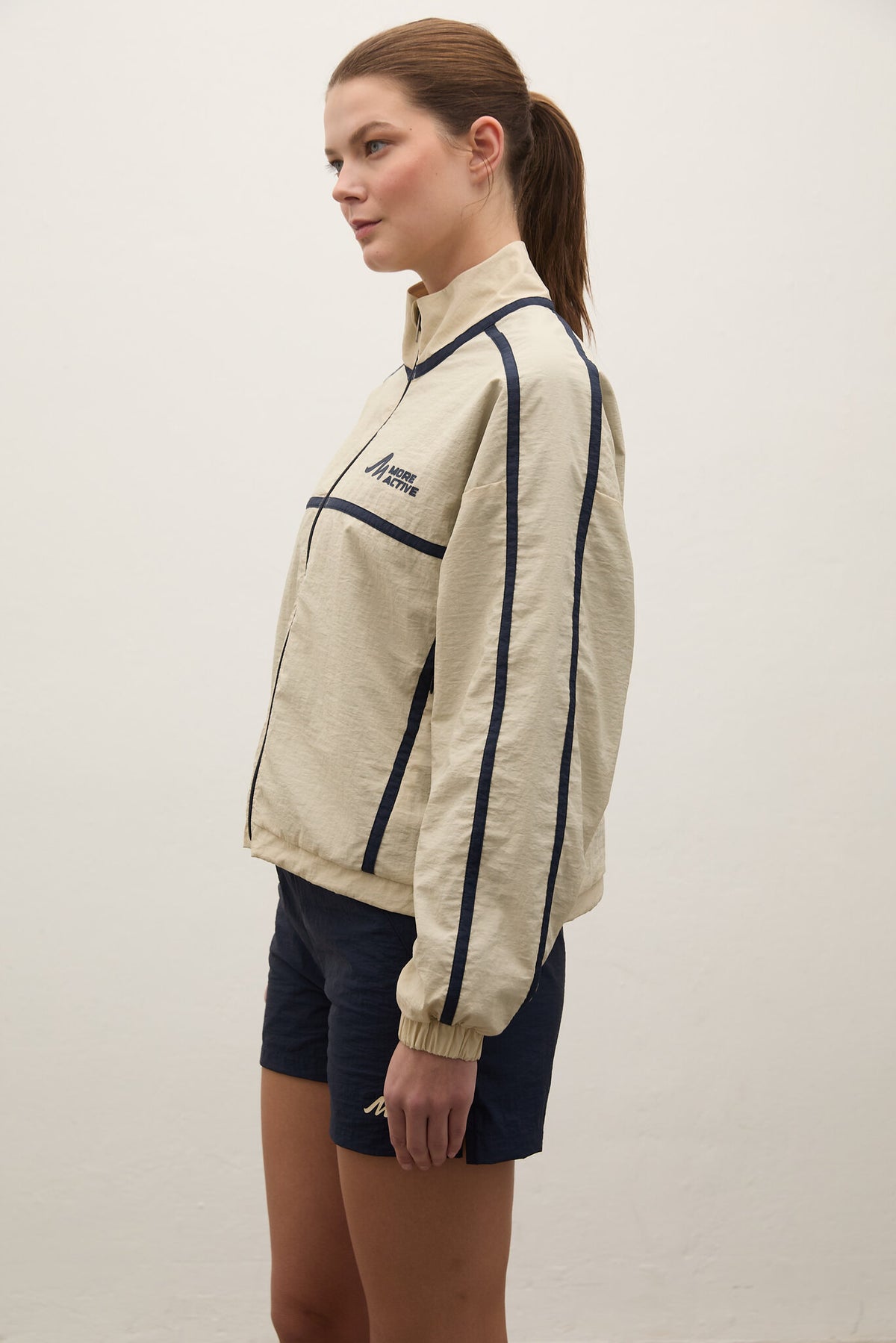 Woman wearing a beige jacket with navy accents on a plain background