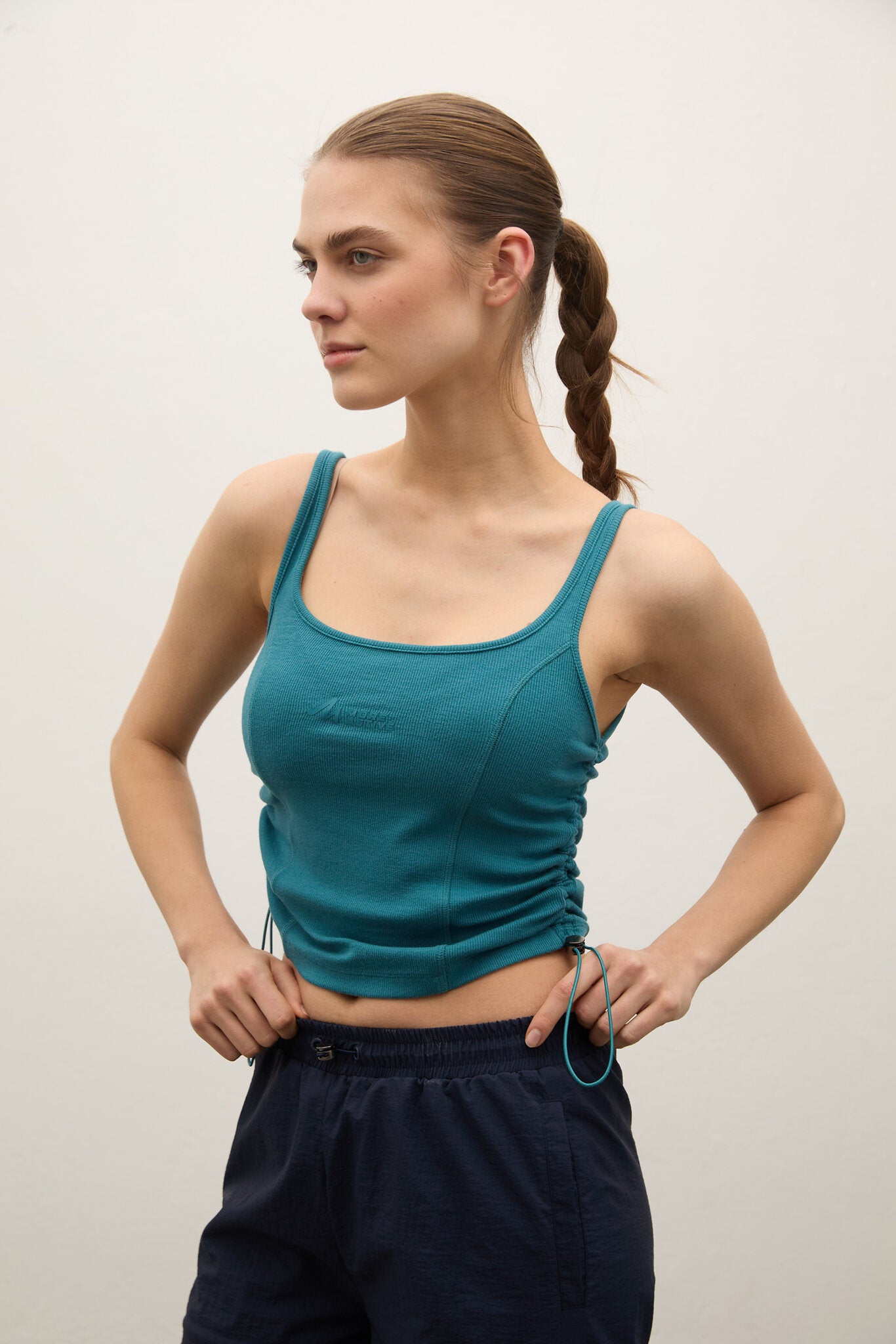 Woman wearing a teal tank top and navy pants against a plain background