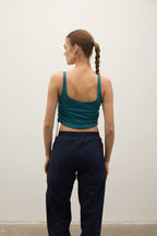 Person wearing a green tank top and navy pants against a white wall