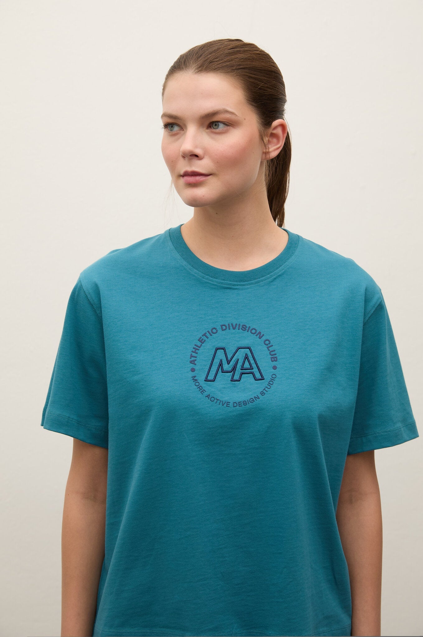 Person wearing a teal t-shirt with a logo on a plain background