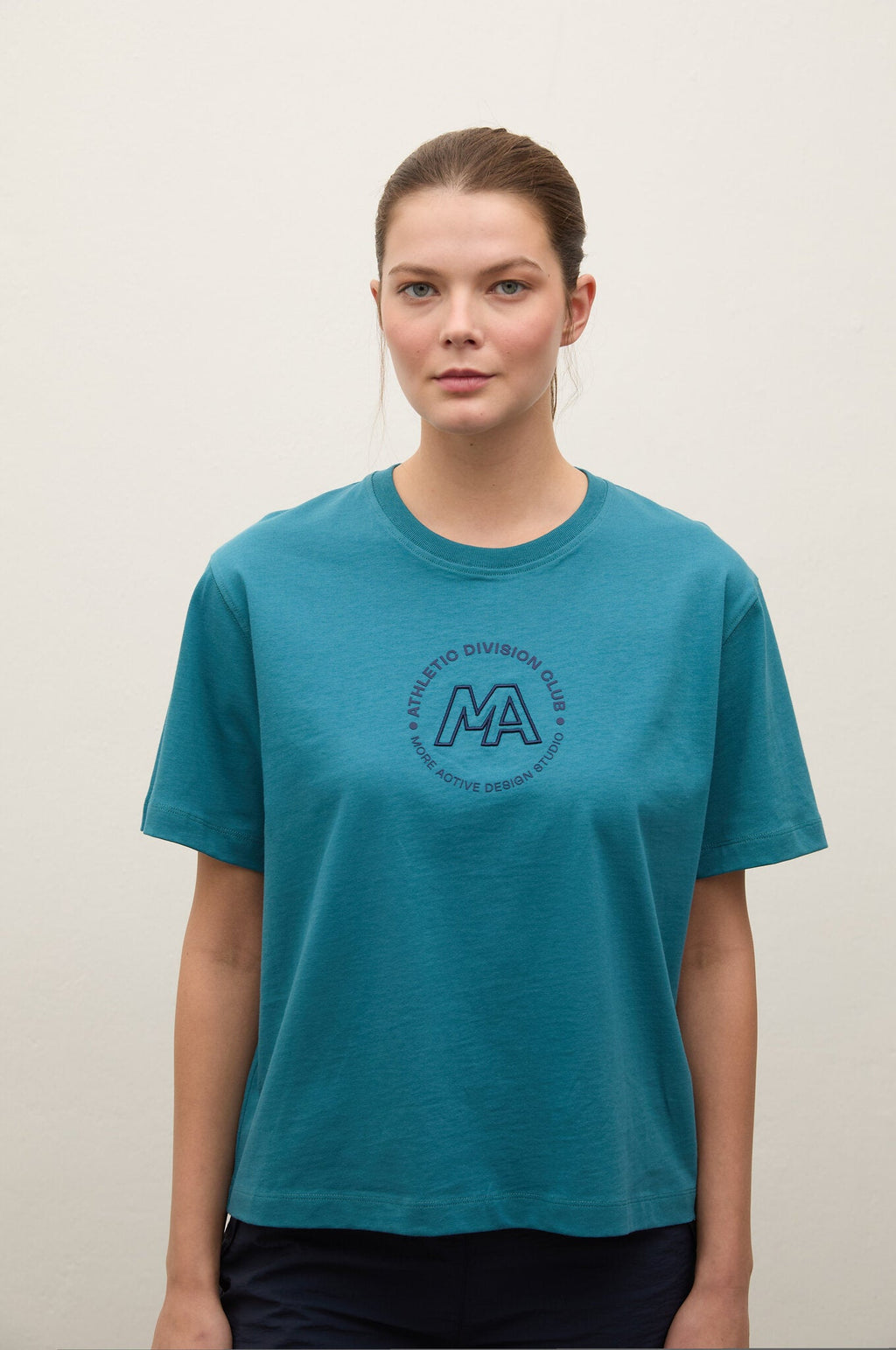 A woman wearing a teal short-sleeve t-shirt with a circular 'Montreal Division 1 A.G.