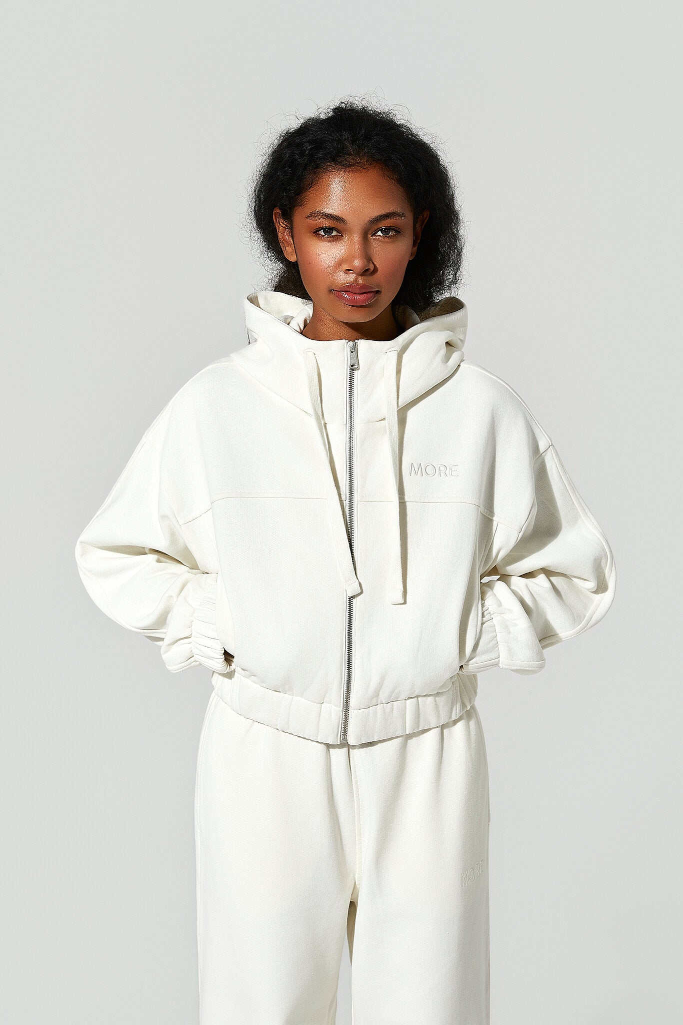 Person wearing a white hoodie and pants on a light gray background