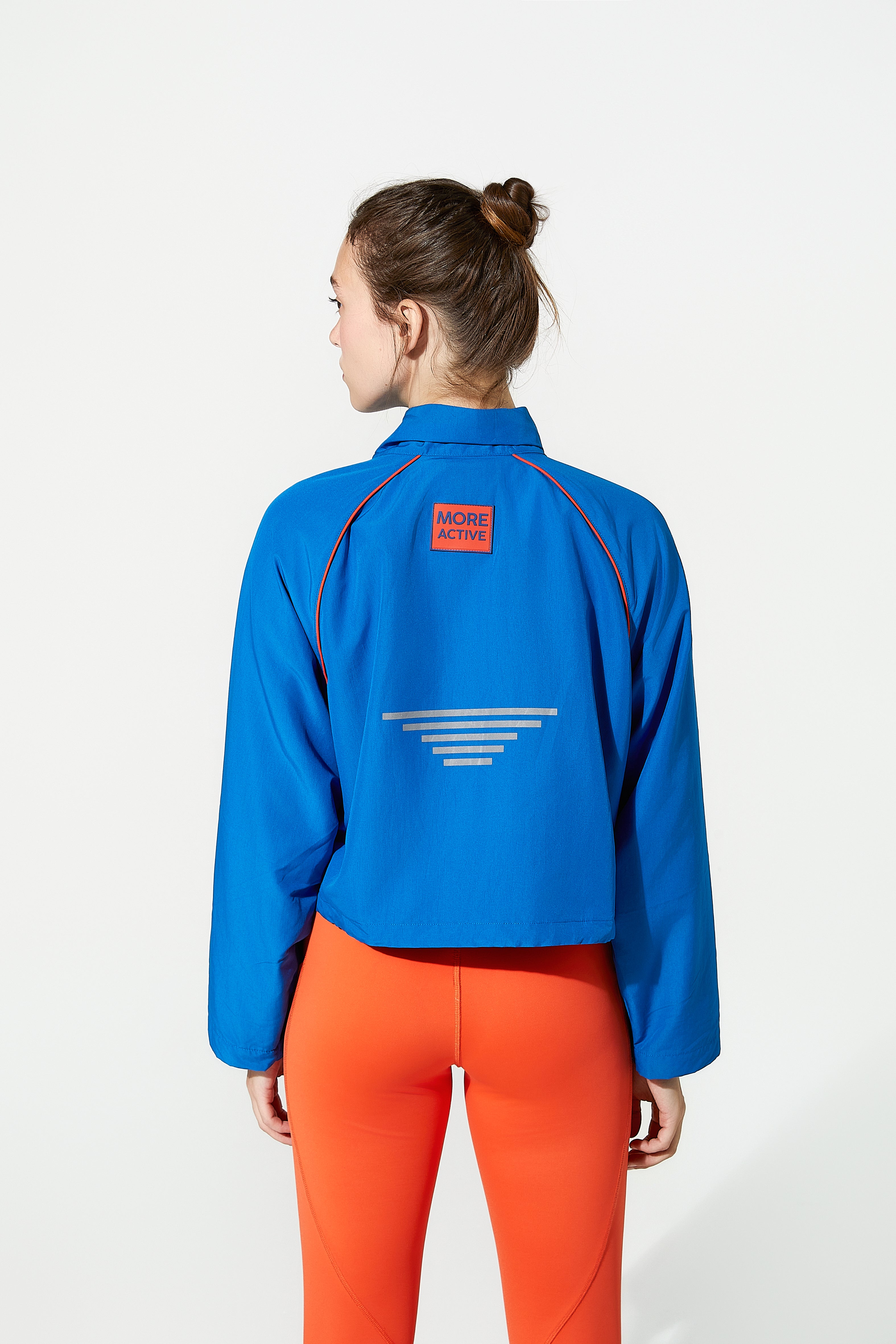 female women wearing a blue cropped jacket with a red logo and orange pants on a white background