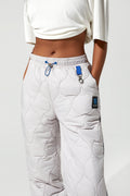 A model wearing white quilted sweatpants with a blue drawstring and a small black brand patch, paired with a white cropped top against a light gray background.