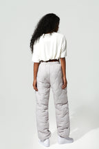 A model shown from the back wearing light gray quilted puffer pants, a white short-sleeve top, and white sneakers against a plain light gray studio background.