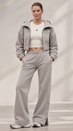 A model wearing a light gray two-piece tracksuit consisting of a cropped hooded jacket and matching wide-leg sweatpants, styled with a white cropped tank top and white sneakers.