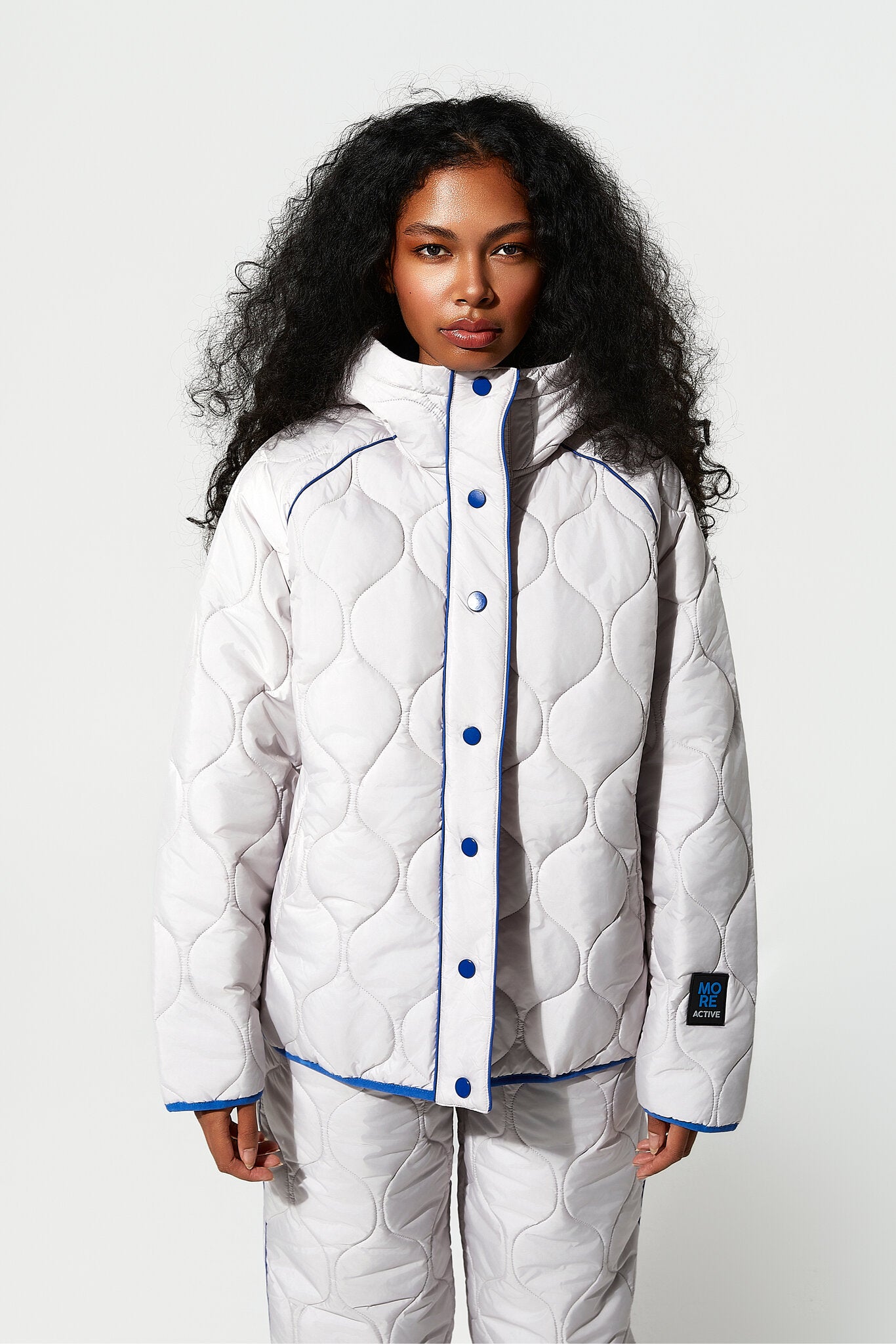 Person wearing a white quilted jacket with blue buttons on a white background