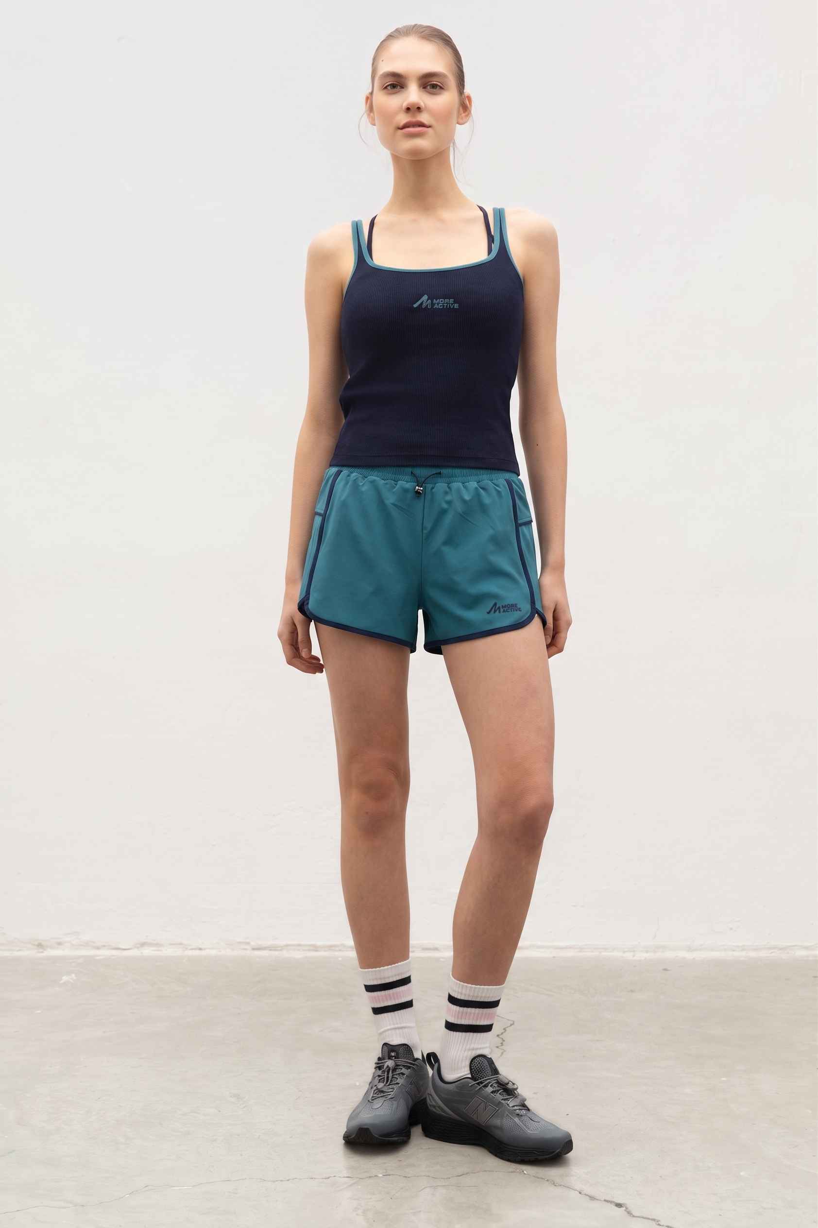 Woman wearing a navy tank top and teal shorts with a white background