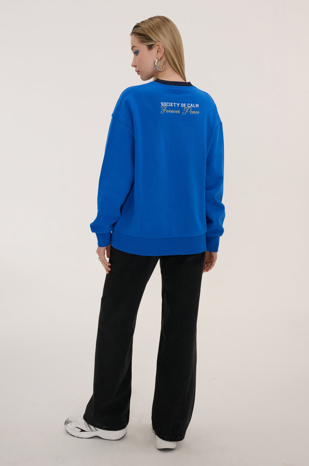 Person wearing a blue sweatshirt with text on the back, standing against a plain background