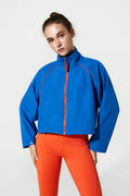 Person wearing a blue jacket with red accents and orange pants on a white background