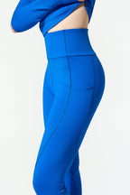 A close-up side view of a model wearing bright royal blue high-waisted leggings with a matching blue cropped top against a plain white background.