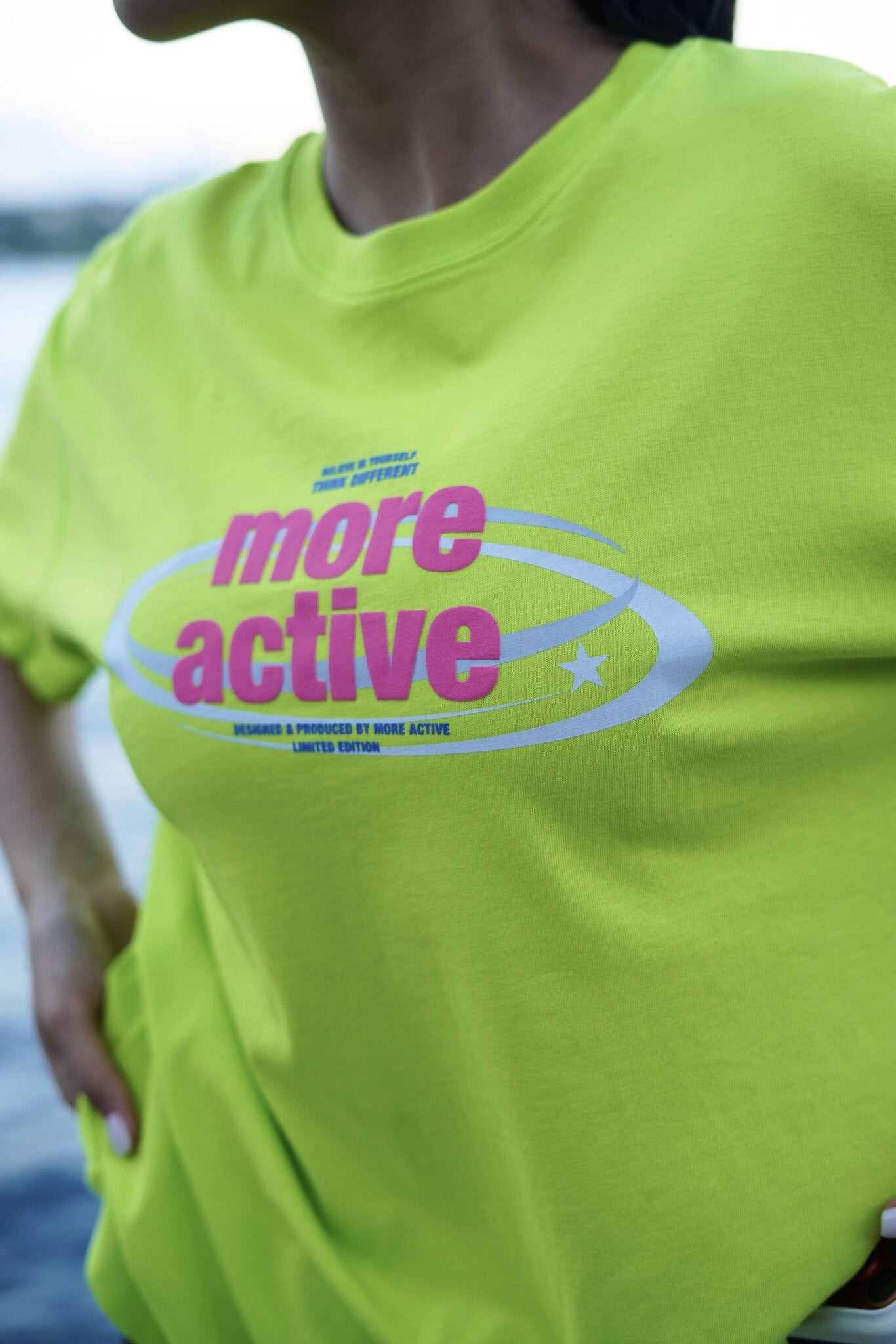 A close-up of a person wearing a bright neon yellow-green t-shirt with a pink and white graphic that reads 'more active' and 'Designed & Produced by More Active'.