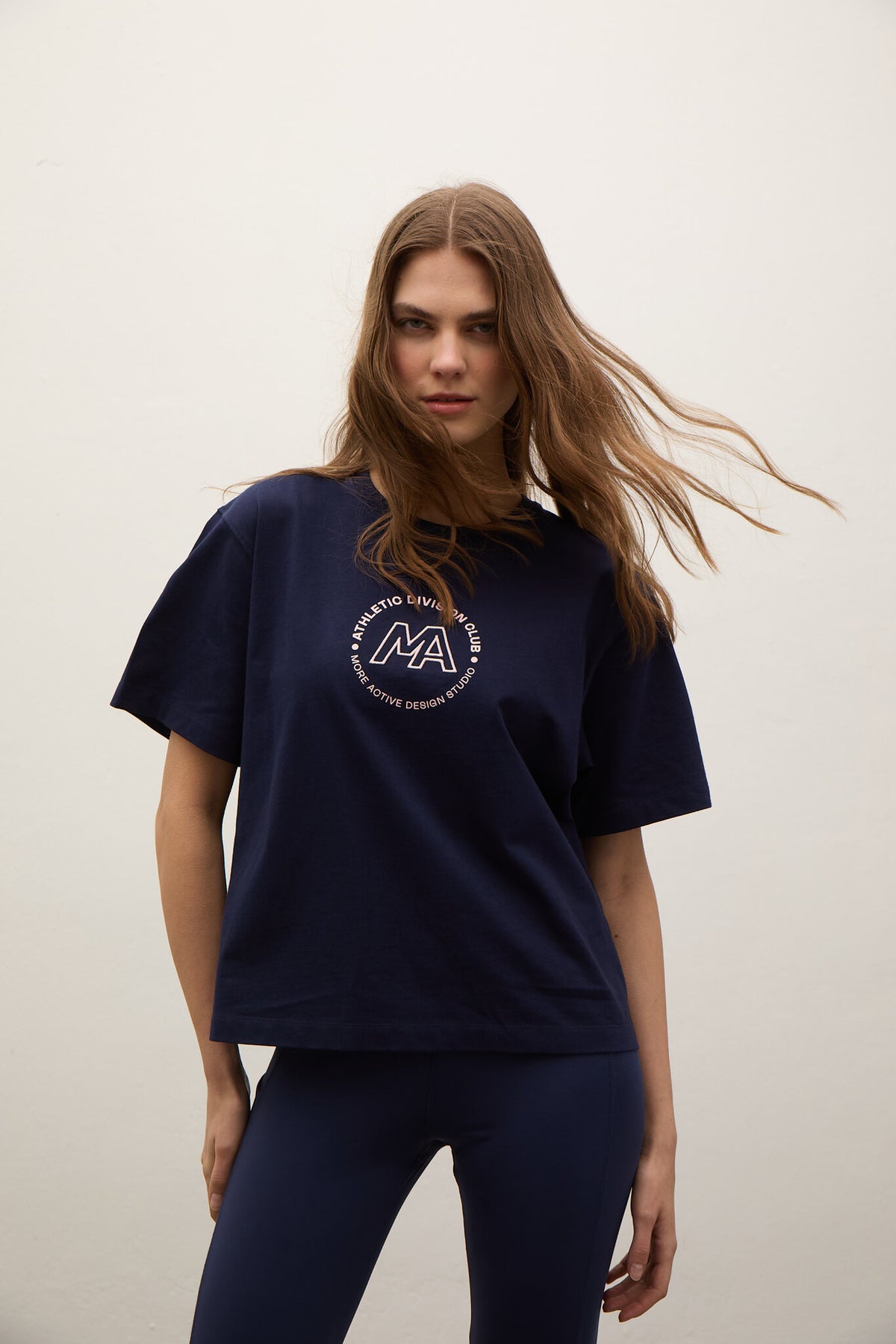 A woman modeling an oversized navy blue t-shirt with a circular white graphic on the chest, paired with matching navy leggings, against a plain off-white background.