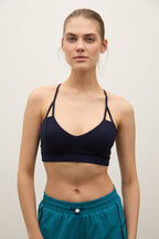 A woman modeling a dark navy blue sports bra with thin straps and teal athletic shorts against a plain light background.
