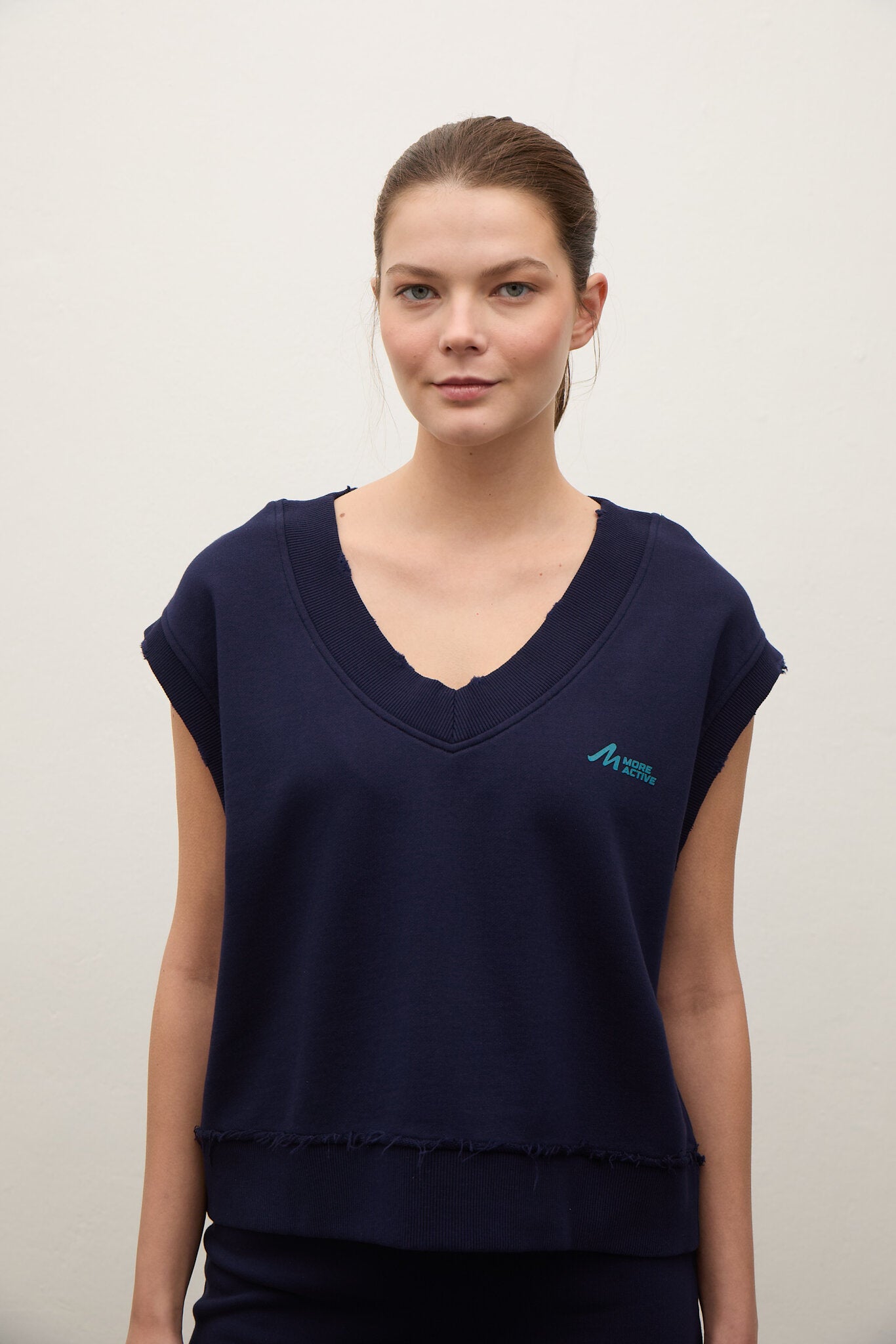 Woman wearing a navy blue top with a logo on a plain background