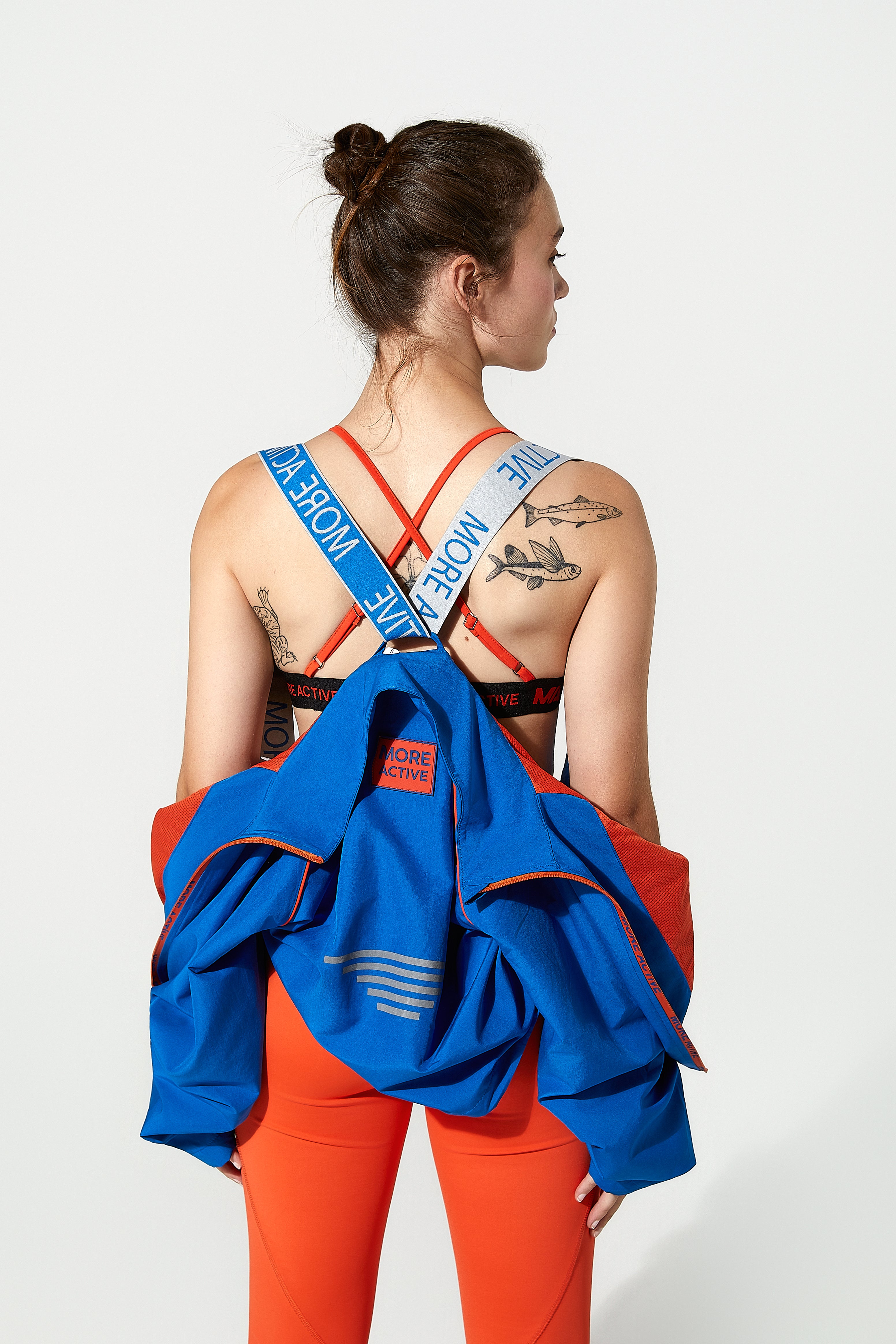 model wearing a blue cropped  jacket over their shoulder with visible tattoos on a white background