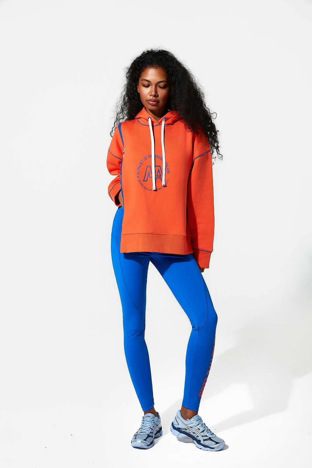 model wearing an orange womens oversized hoodie​ and blue leggings on a white background