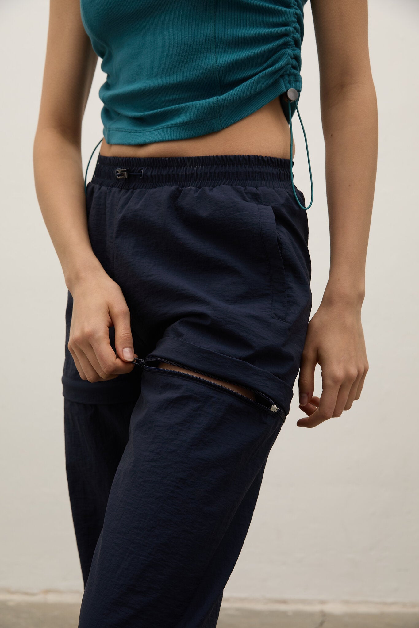 Person wearing navy pants and a teal top against a neutral background