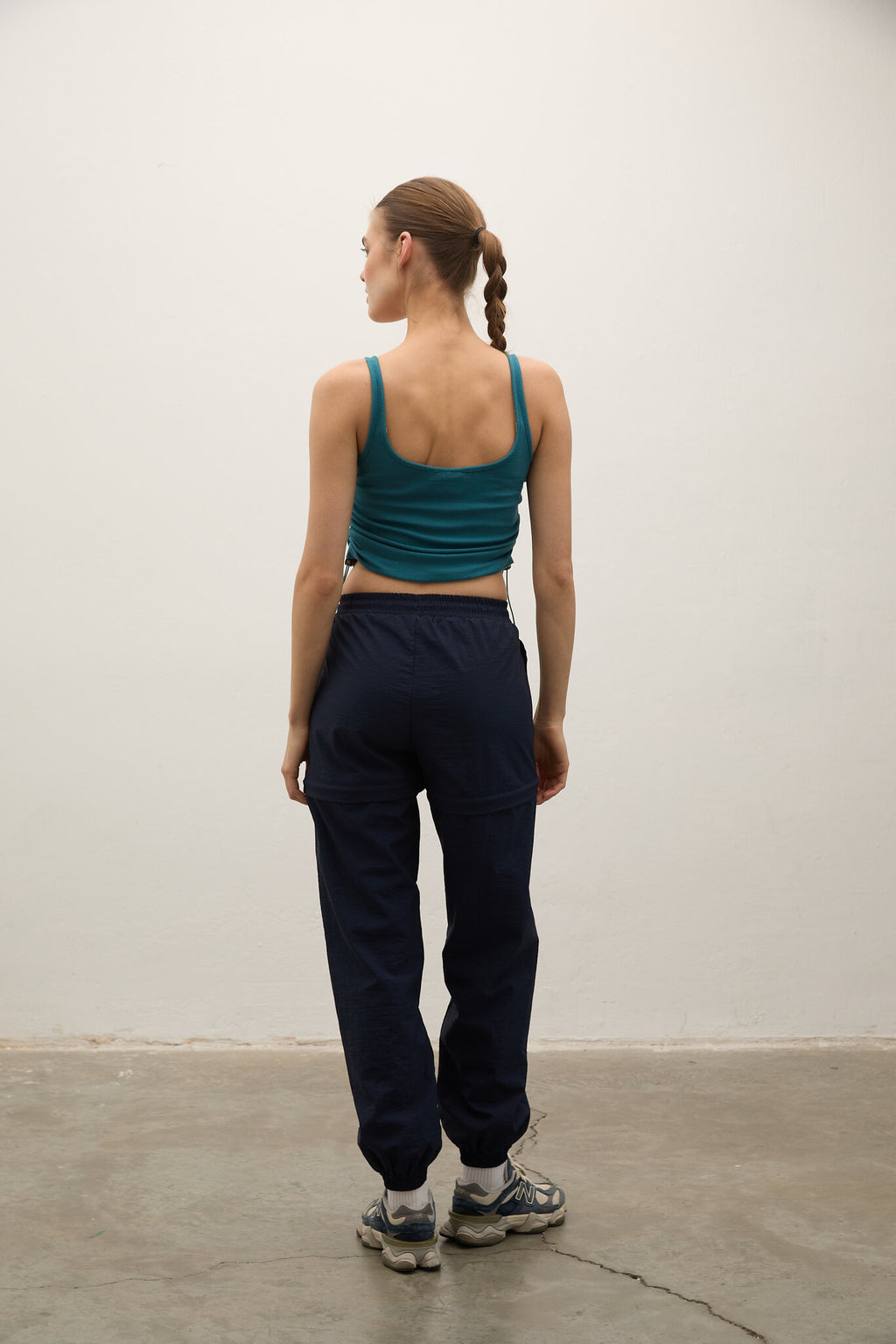 Person wearing a green tank top and navy pants standing against a plain white wall.