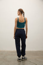 Person wearing a green tank top and navy pants standing against a plain white wall.