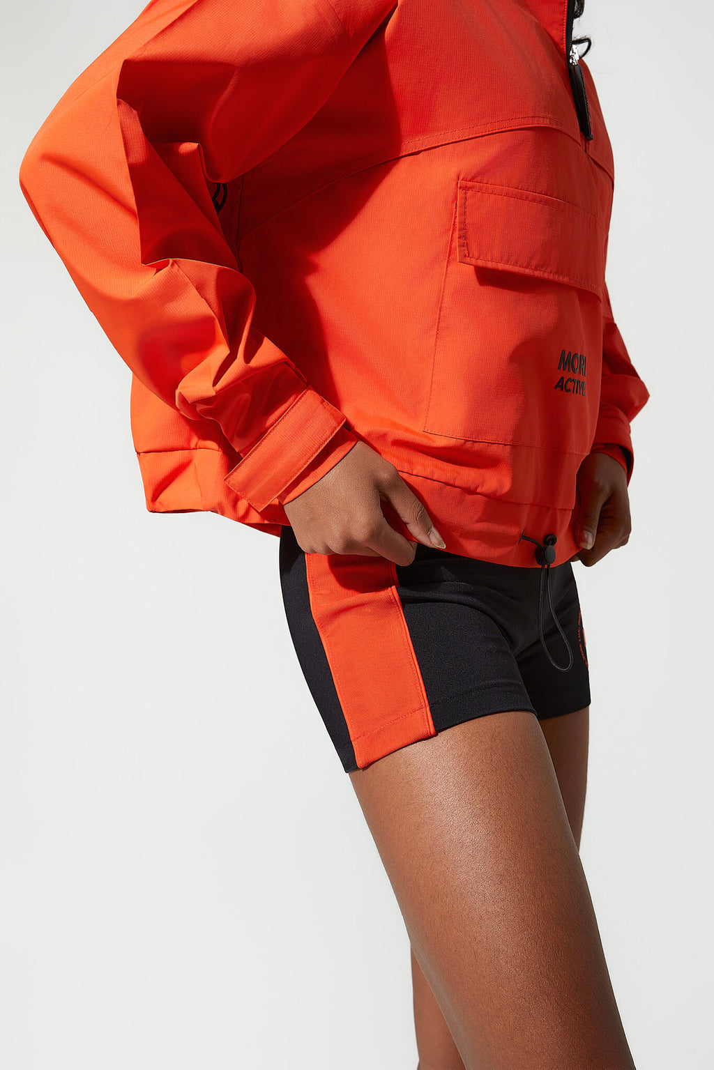 Person wearing an orange jacket and black shorts on a white background