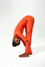 A model wearing a bright orange Gym Leggings is posed in a deep forward bend on a seamless white studio background.