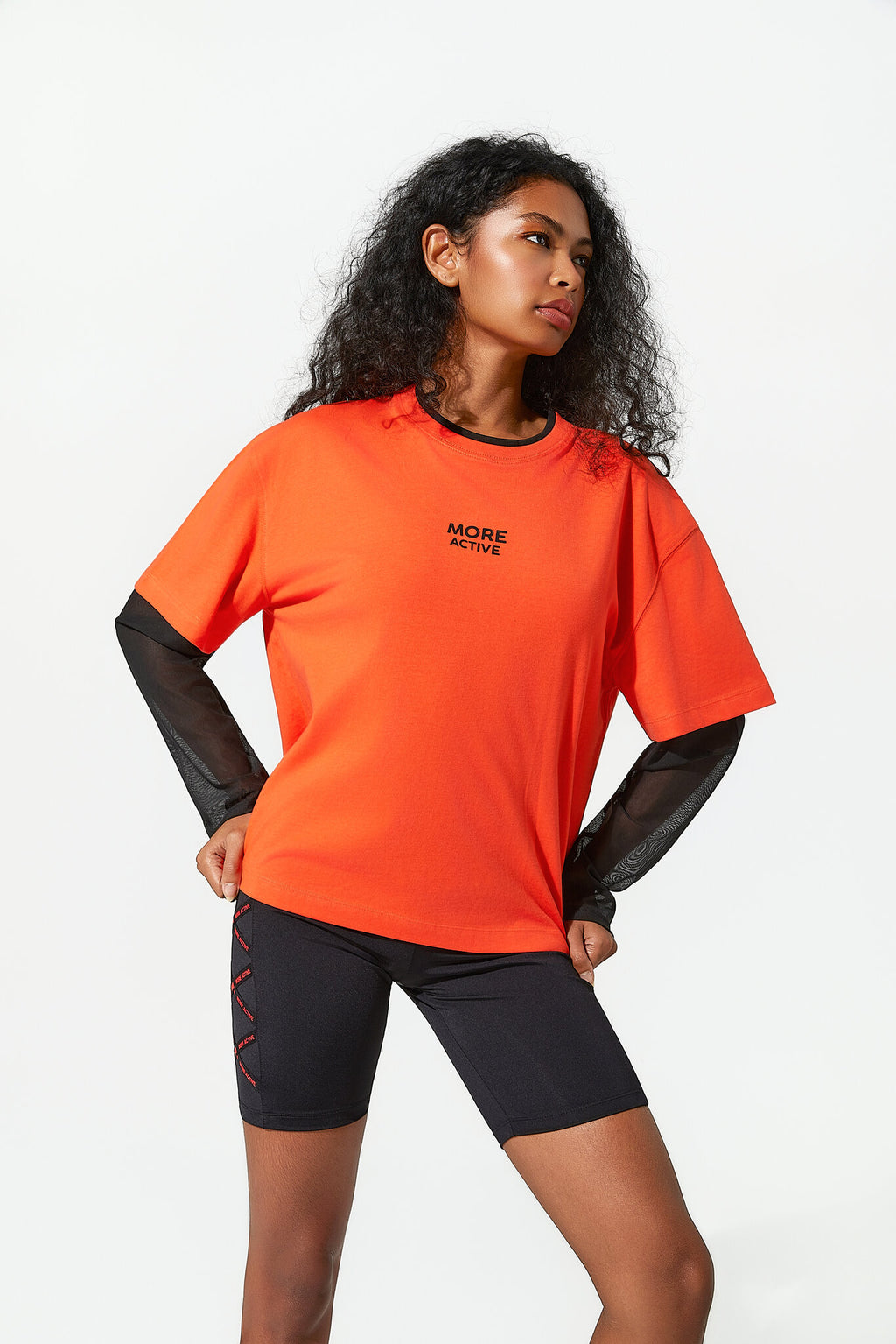 Woman wearing an orange athletic shirt with black sleeves and black shorts on a white background