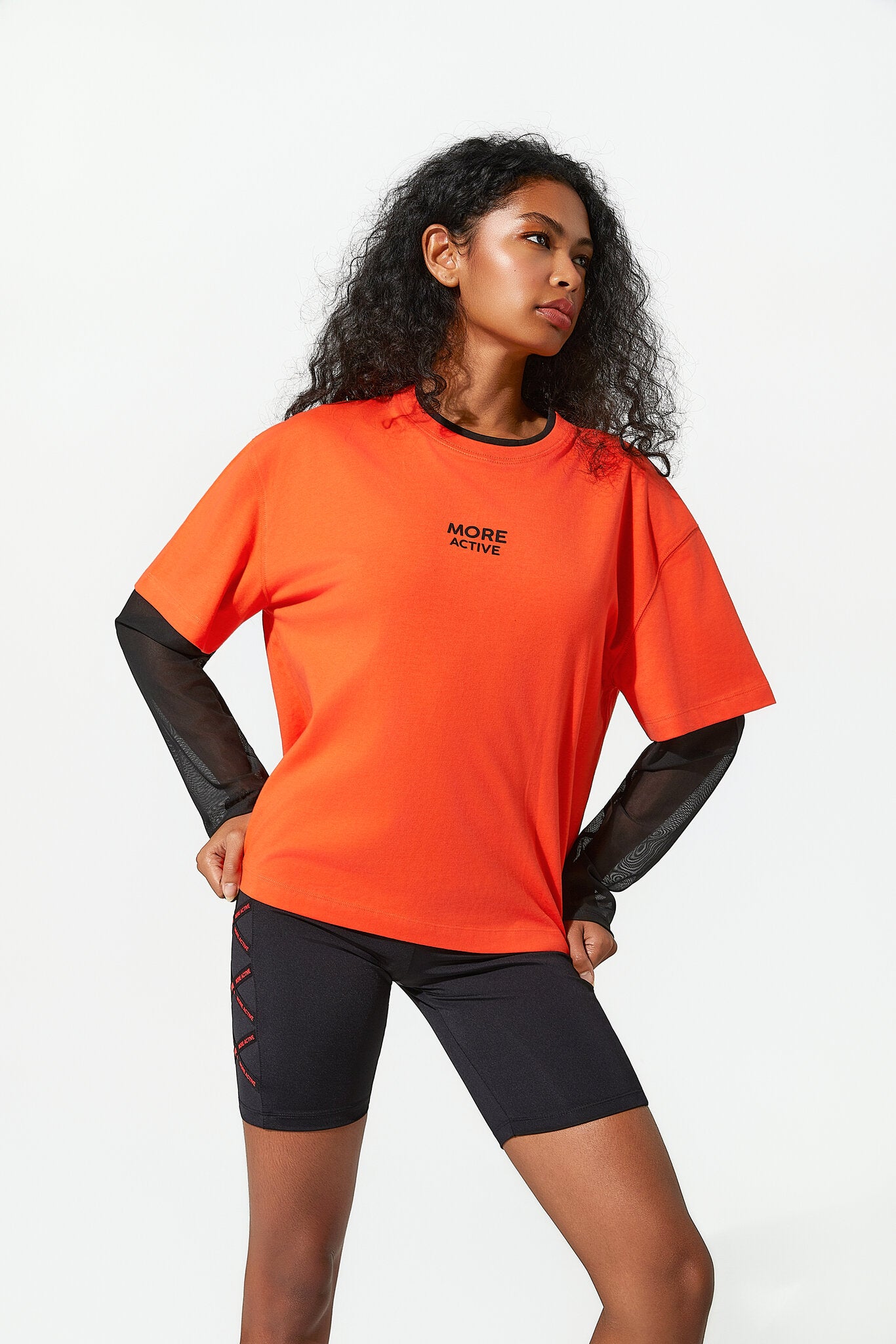 Woman wearing an orange athletic shirt with black sleeves and black shorts on a white background