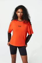 Woman wearing an orange athletic shirt with a brand logo on a white background