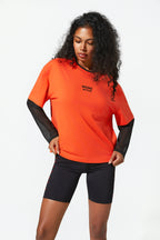 Woman wearing an orange athletic shirt and black shorts on a white background