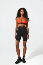 Woman wearing an orange sports bra and black shorts on a white background