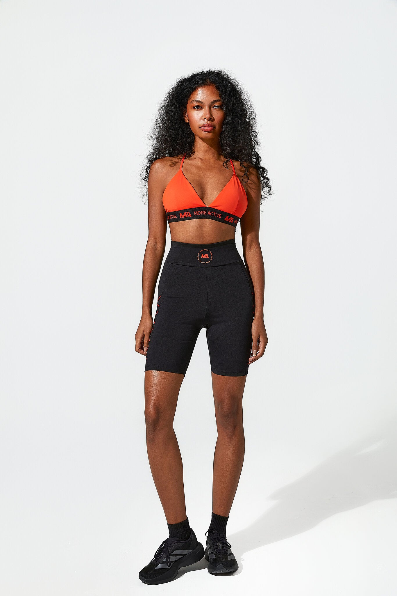 Woman wearing an orange sports bra and black shorts on a white background