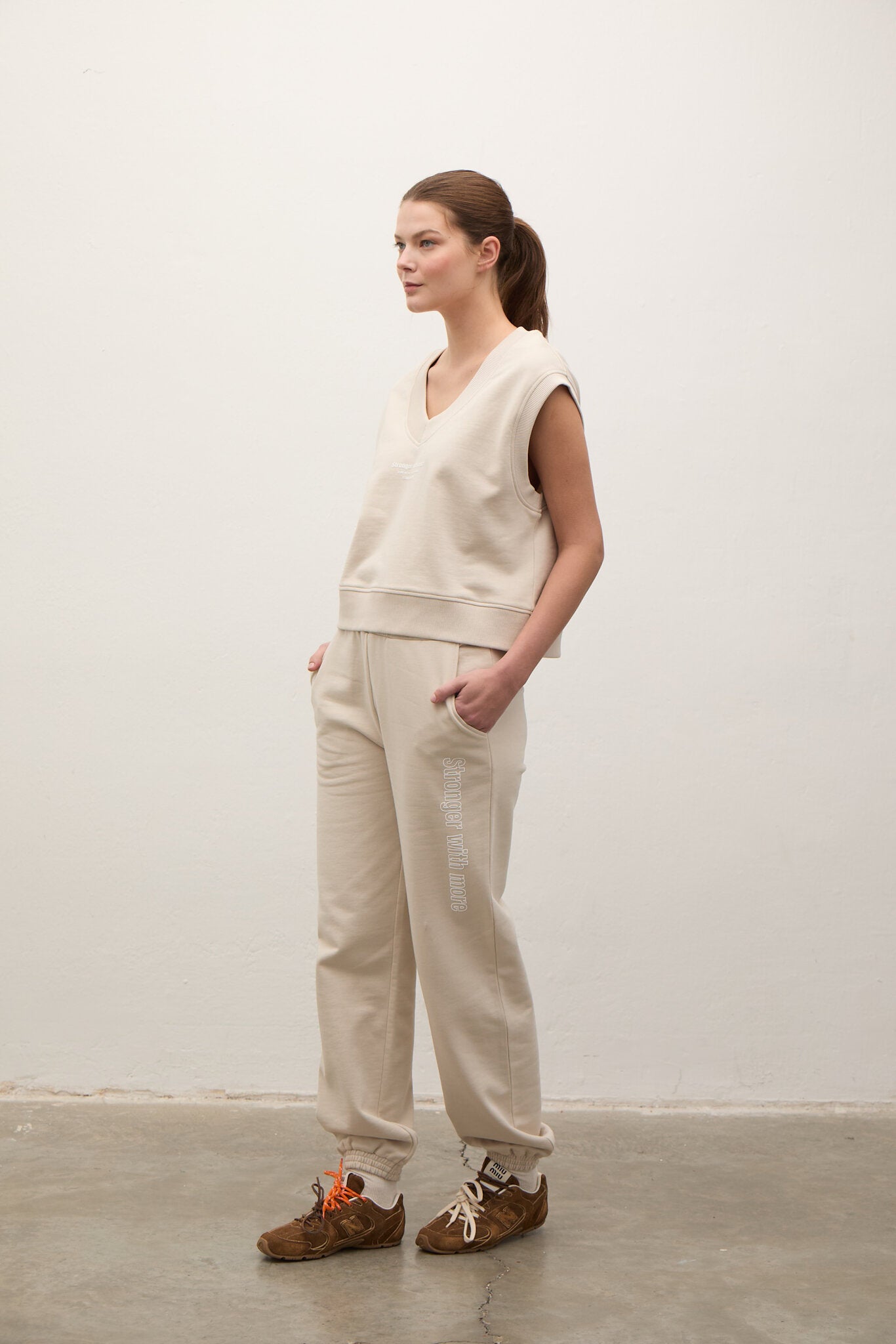 Woman wearing a beige sleeveless top and pants against a white background