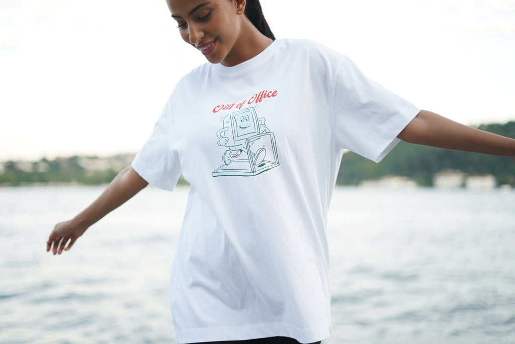 A woman wearing an oversized white graphic t-shirt with a 'Chair of Alice' typewriter design, posing outdoors with a blurred lake and trees in the background.