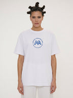 A model wearing a white short-sleeve t-shirt with a blue circular graphic on the chest that reads 'A LIFELONG DIVISION CLUB' around a large 'MA' monogram, paired with white pants against a plain light background.